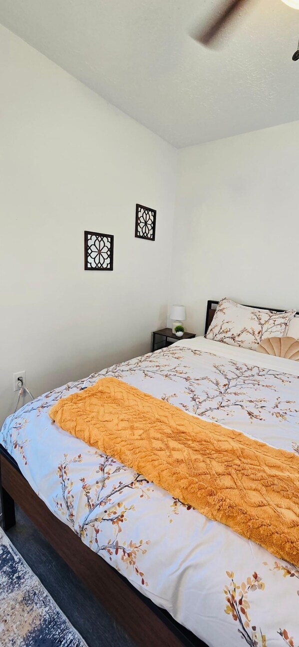 Un dormitorio con una cama, una mesita de noche, una lámpara y dos adornos colgados en la pared.