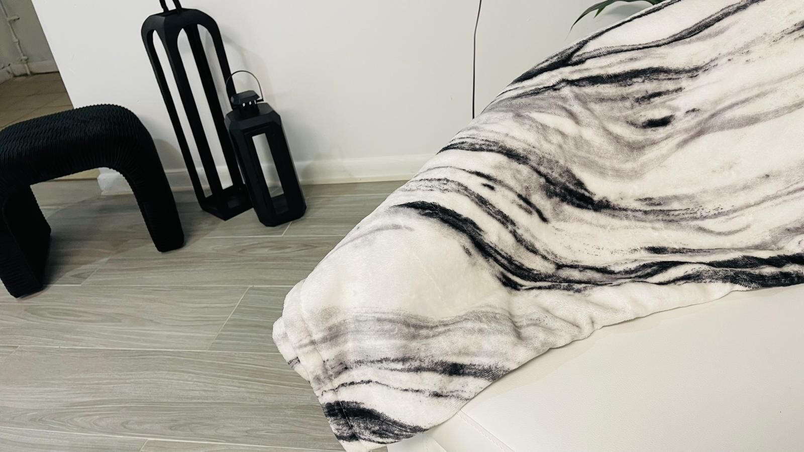 Een kamer met een witte bank, een zwarte stoel en een zwarte lantaarn op de vloer.