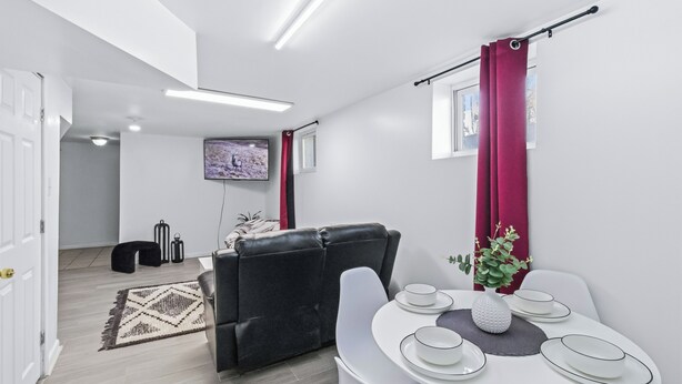 A modern living room with a black leather sofa, a dining table set with white plates and a vase, and a TV mounted on the wall.