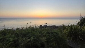 A coastal landscape with a sunset over the water, foreground vegetation, and a clear sky. - Seaside Chalet with Direct Water Access (Fermanville)