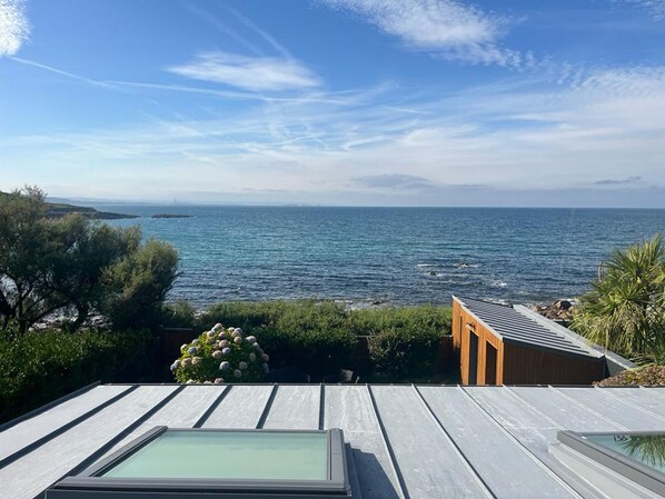 Une terrasse avec vue sur la mer, une plateforme en bois et une véranda vitrée.