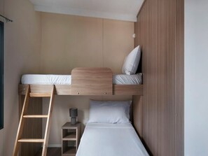 A bunk bed with a ladder, a bedside table with a lamp, and a wall-mounted shelf.
