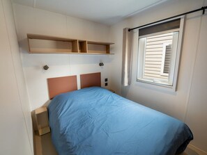 A bedroom with a bed, a window with blinds, and built-in shelves above the bed. - Mobile Home 6 Pers - Terrace - Granges-Aumontzey (Granges-Aumontzey-Aumontzey)