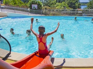 A swimming pool with people in the water and a child on a slide.