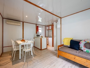 A compact room with a wooden-framed bed, a dining table with chairs, a kitchenette, and a small bathroom.