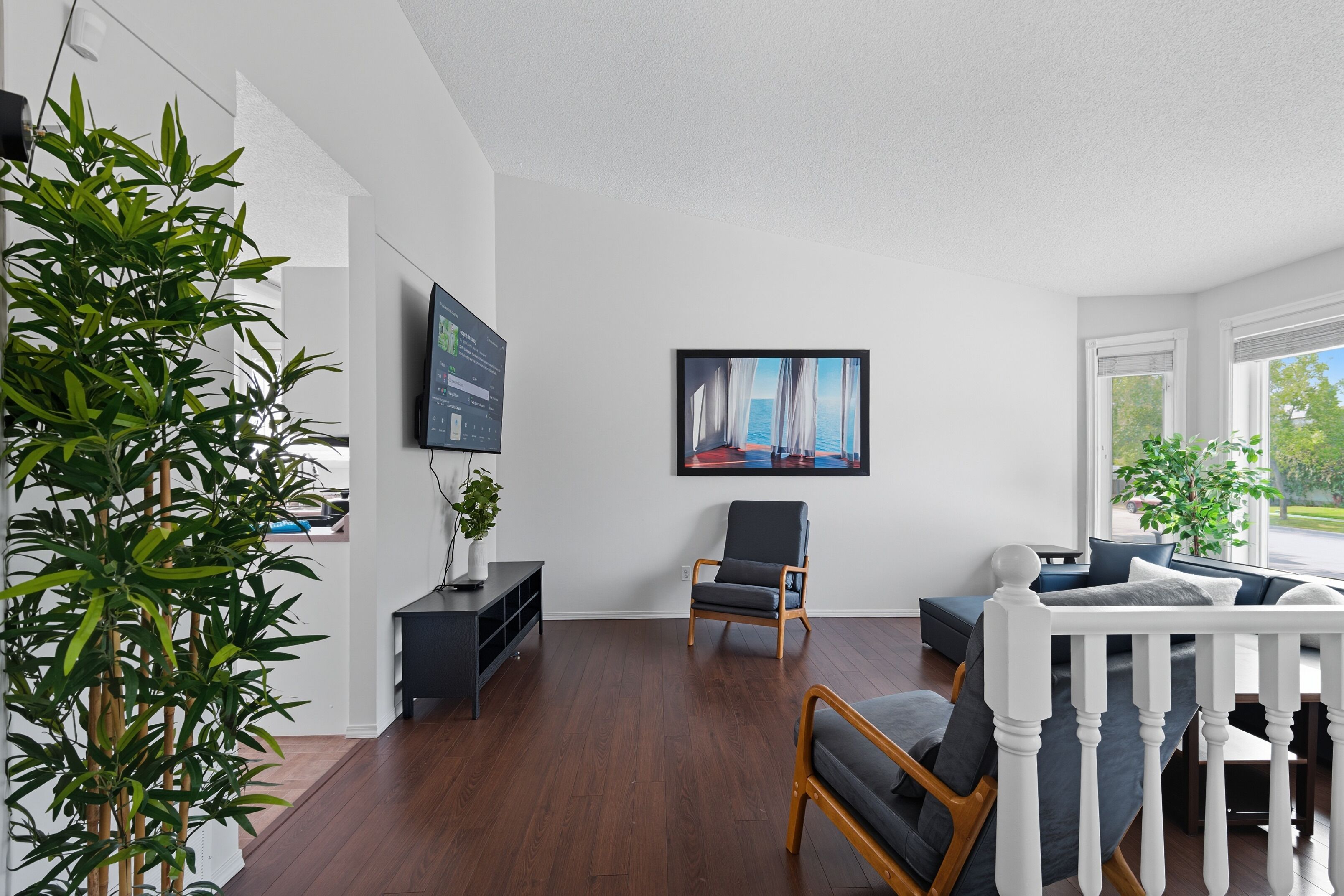 A modern living room with a wooden floor, a black armchair, a grey sofa, and a white railing.