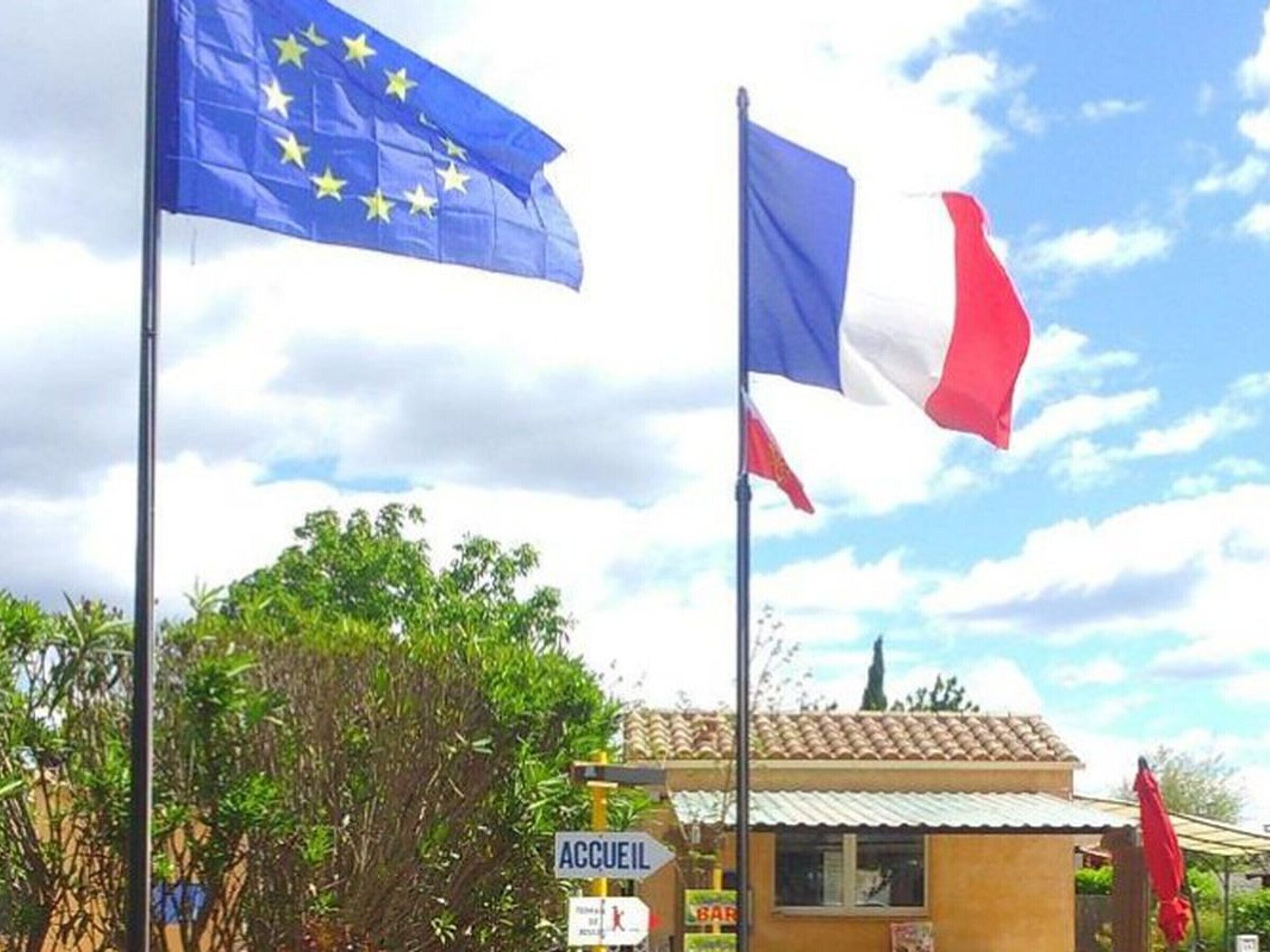 Two flags, one of the European Union and one of France, with a sign for 'ACCUEIL' in the foreground.