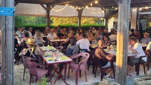 Un espace de restauration en plein air, équipé de tables et de chaises, de guirlandes lumineuses et doté d’une structure de toit abritée.