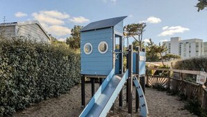 A playground with a blue slide and climbing structure, surrounded by sand and greenery. - Spacious mobile home 6 people, terrace (Saint-Michel-Chef-Chef)