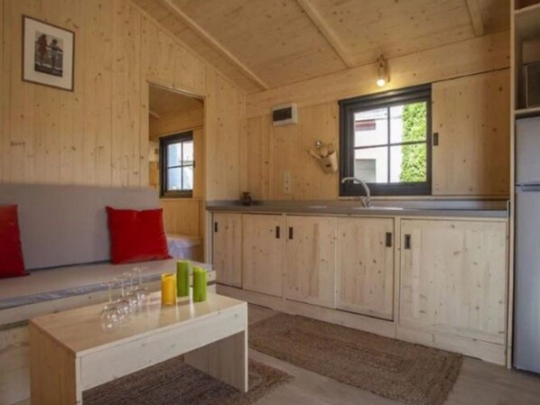 A cozy cabin interior with a wooden interior, a dining area with a table and chairs, a kitchen with a sink and cabinets, and a window providing natural light. - 30m² Chalet with Terrace and Safe (Le Fouilloux)