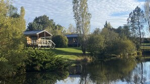 Un chalet au bord du lac, doté d’une terrasse et d’un porche abrité, entouré d’arbres et bordé par une étendue d’eau calme.