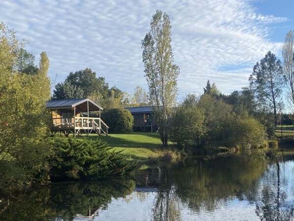 Uma cabana à beira do lago com varanda e alpendre coberto, rodeada por árvores e águas calmas.