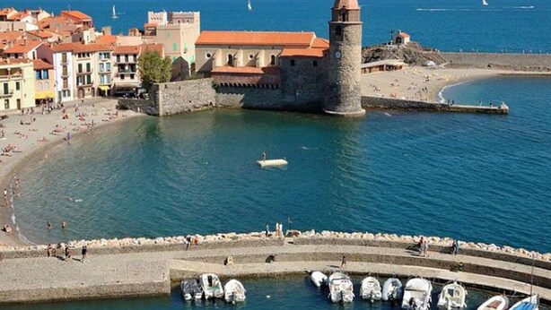 A coastal town with a prominent tower, a sandy beach, and a marina with boats.
