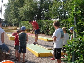 Ein Freizeitbereich im Freien, in dem ein Mann ein Spiel zeigt, umgeben von Kindern, die zusehen.