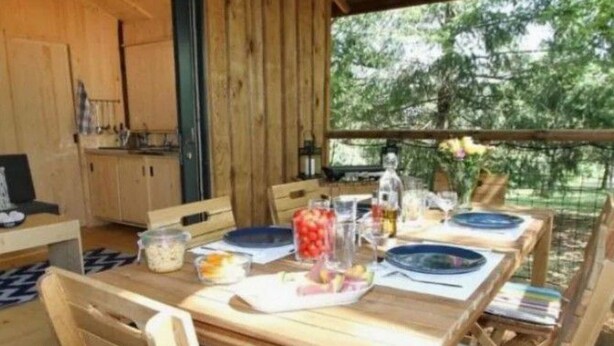 A wooden deck with a table set for dining, surrounded by chairs with colorful cushions.