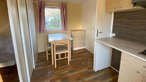 A compact kitchen with a dining table and chairs, a built-in oven, and a window with curtains.