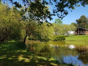 Eine rustikale Holzhütte mit einer Holzterrasse, umgeben von üppigem Grün und einem stillen Teich.