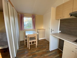 A compact kitchen with a dining table and chairs, a window with curtains, and a built-in oven.