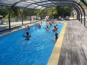 A swimming pool with a covered area, surrounded by trees and a wooden deck.