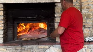 A person in a red shirt using a long-handled tool to manage a fire in a stone-built oven.