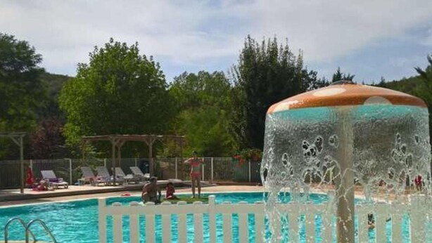 A swimming pool with a water fountain feature, surrounded by a white fence and lounge chairs.