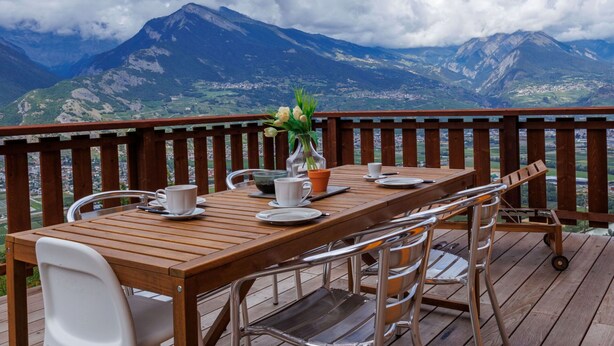 Eine Holzterrasse mit einem Tisch für zwei Personen, mit Blick auf eine gebirgige Landschaft.