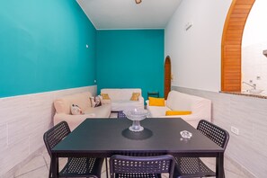 A dining area with a black table and chairs, a white sofa with yellow cushions, and a teal accent wall.
