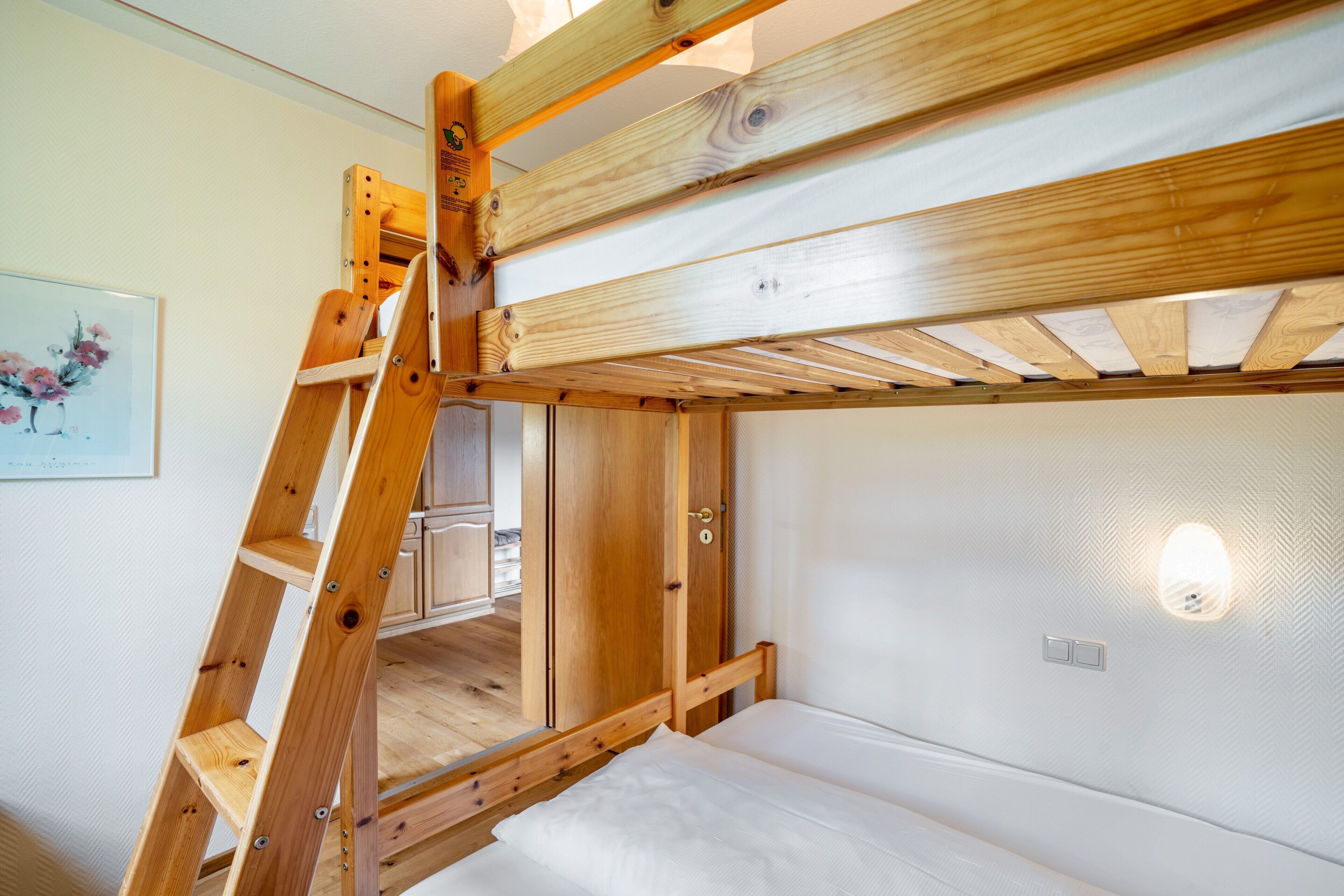 A bunk bed with a wooden ladder, a white wall, and a light fixture.