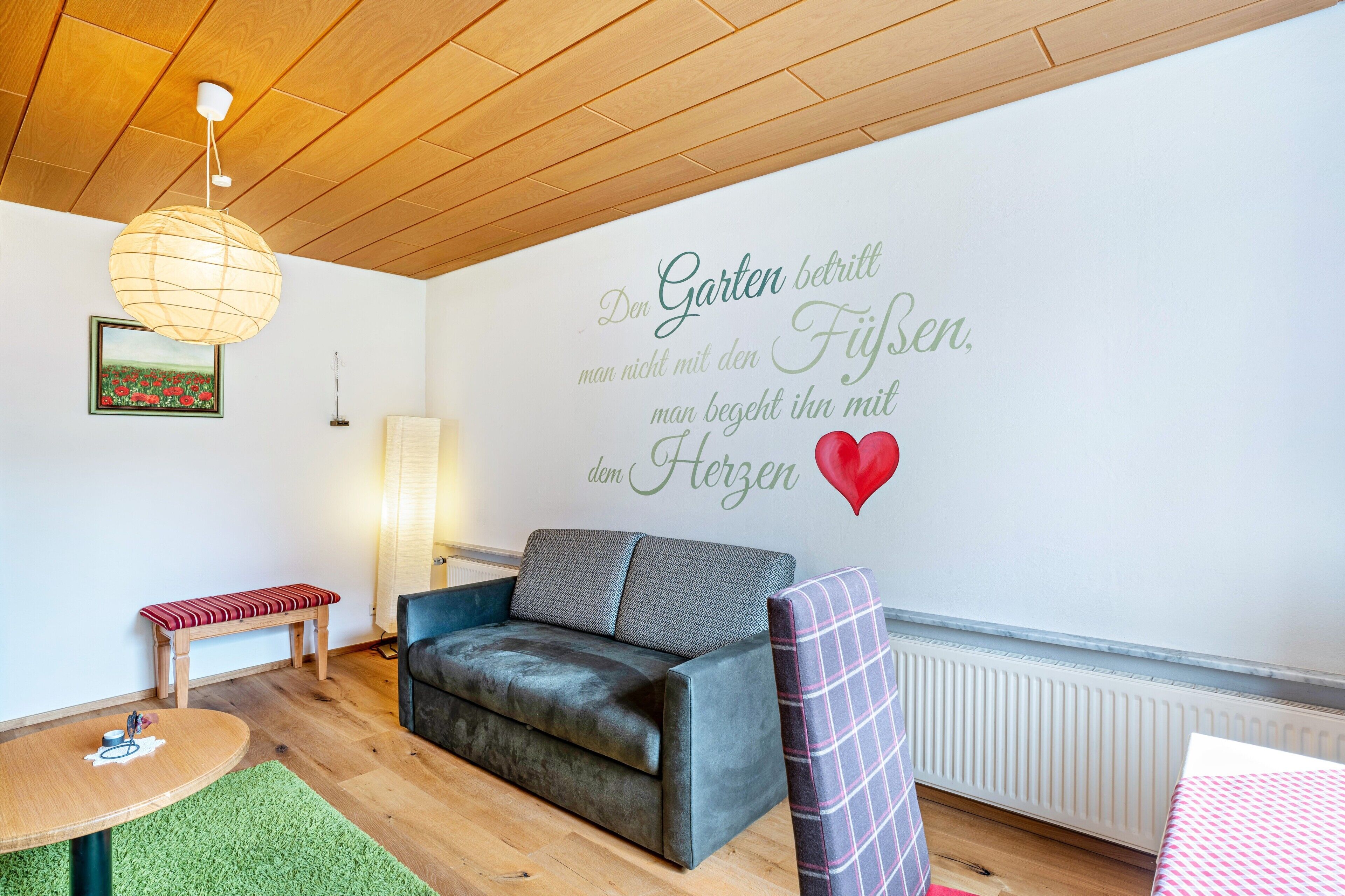 A cozy living room with a leather sofa, a bench, a round table, and a wall with a German quote.