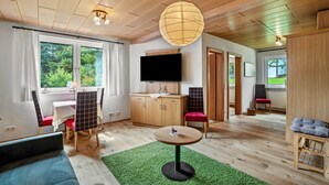 Una habitación con techo de madera, televisor, una mesa de comedor con sillas, alfombra verde y un sofá.