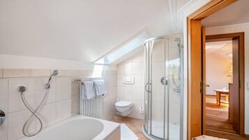 Une salle de bain moderne équipée d’une baignoire, d’une douche, de toilettes et d’un espace douche séparé par des parois en verre.