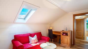 A red sofa, a small round table, a wooden cabinet, a desk, and a skylight in a room with wooden flooring.
