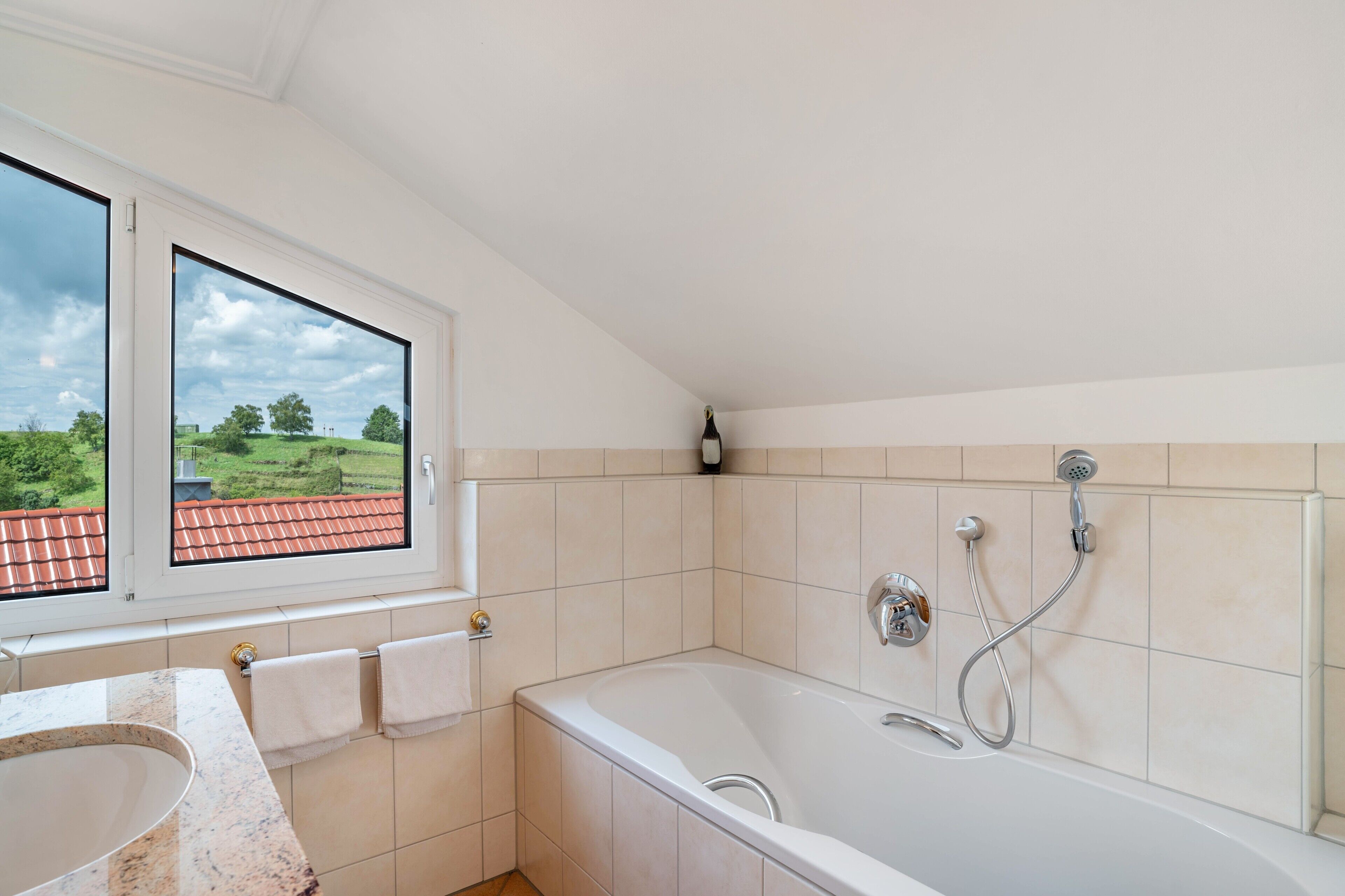 Un baño con bañera, ventana con vista a la vegetación y pared de azulejos.
