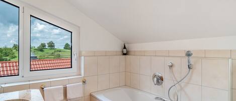 Un baño con bañera, ventana con vista a la vegetación y pared de azulejos.