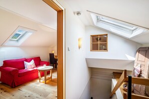 Une pièce de style loft avec un canapé rouge, une petite table, une lucarne et un escalier.