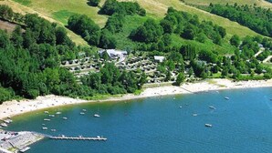 An aerial view of a coastal area with a marina, boats, and a residential area with houses and greenery. - Cottage for 5 with lakeside terrace (Salles-Curan)