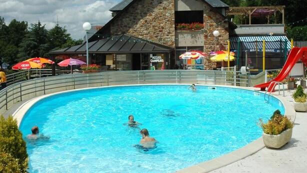 A swimming pool with people in it, surrounded by umbrellas and a building with a stone facade. - Cottage for 5 with lakeside terrace (Salles-Curan)