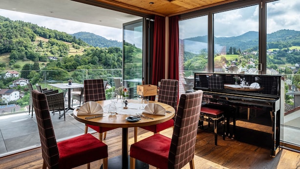 A dining area with a piano, red upholstered chairs, a round table, and a scenic mountain view through large windows. - Country House Room 'Lebensfreude' with Mountain View and Wi-Fi (Bühlertal)