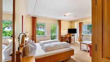 A bedroom with a wooden bed, a desk, a chair, a TV, and large windows.