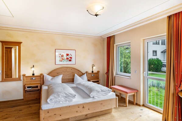 A bedroom with a wooden bed, bedside tables, a bench, a window with a view, and a ceiling light fixture.