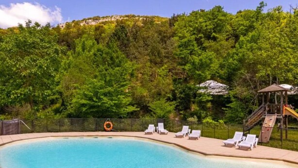 Ein Swimmingpool mit Liegestühlen und einer Rutsche, umgeben von Bäumen.