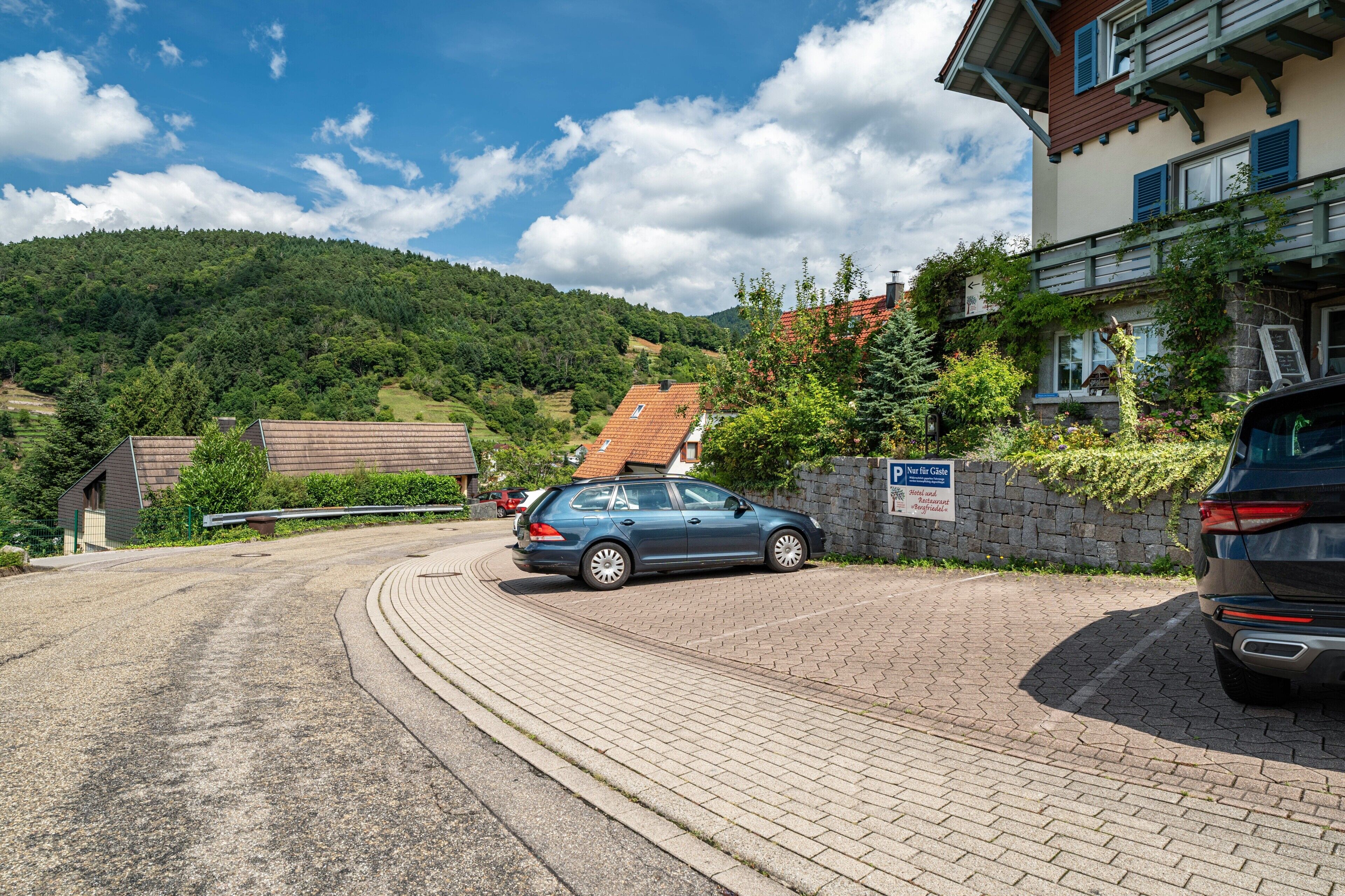 Een woonwijk met een verharde oprit, een geparkeerde auto en een huis met een schuin dak en een stenen muur.