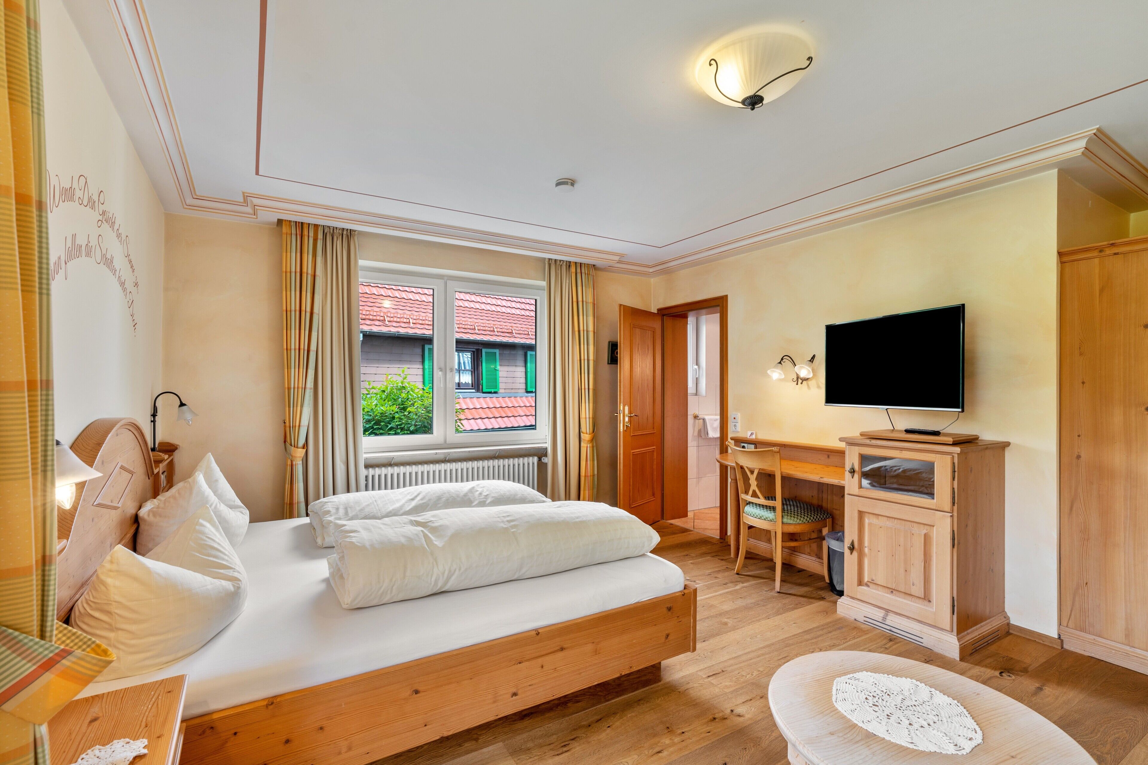A bedroom with a bed, a television, a desk, and a view of a building outside.