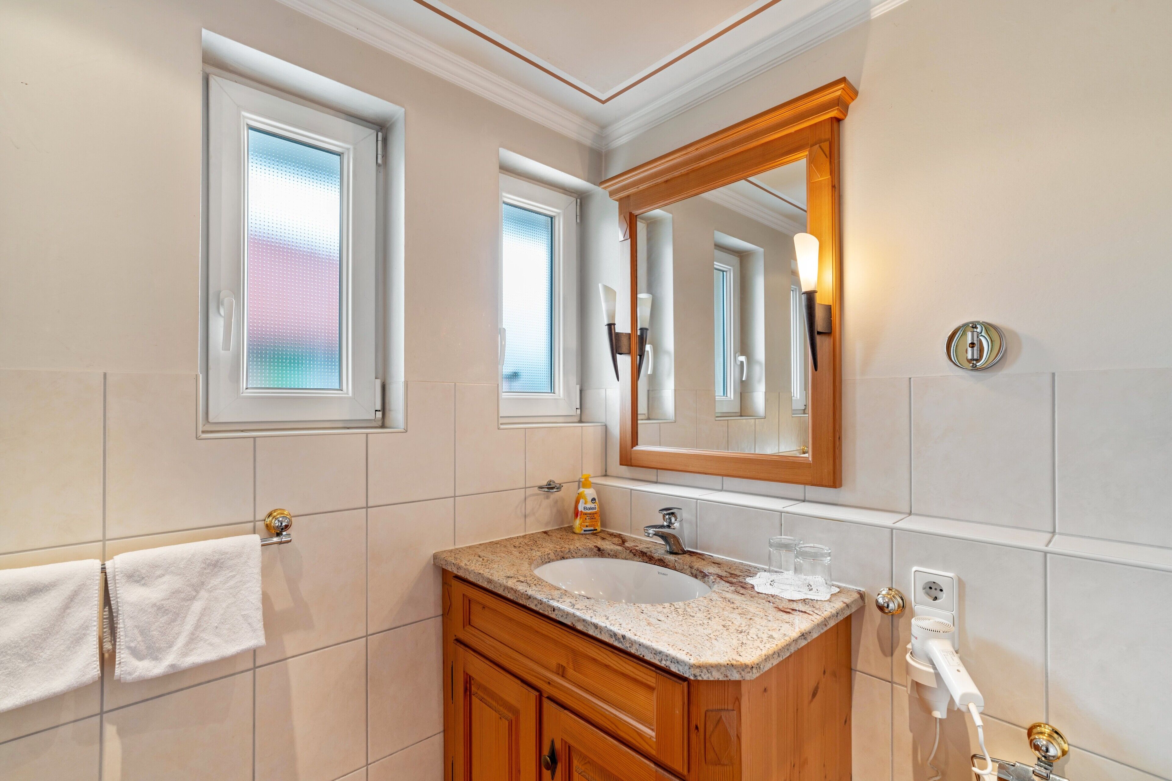 Ein Badezimmer mit Waschbecken, Waschtisch, Spiegel, Handtuchhalter und einem Fenster mit Milchglas.
