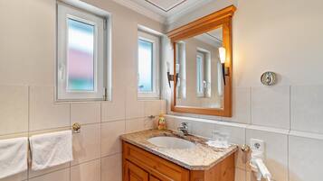 Ein Badezimmer mit Waschbecken, Waschtisch, Spiegel, Handtuchhalter und einem Fenster mit Milchglas.