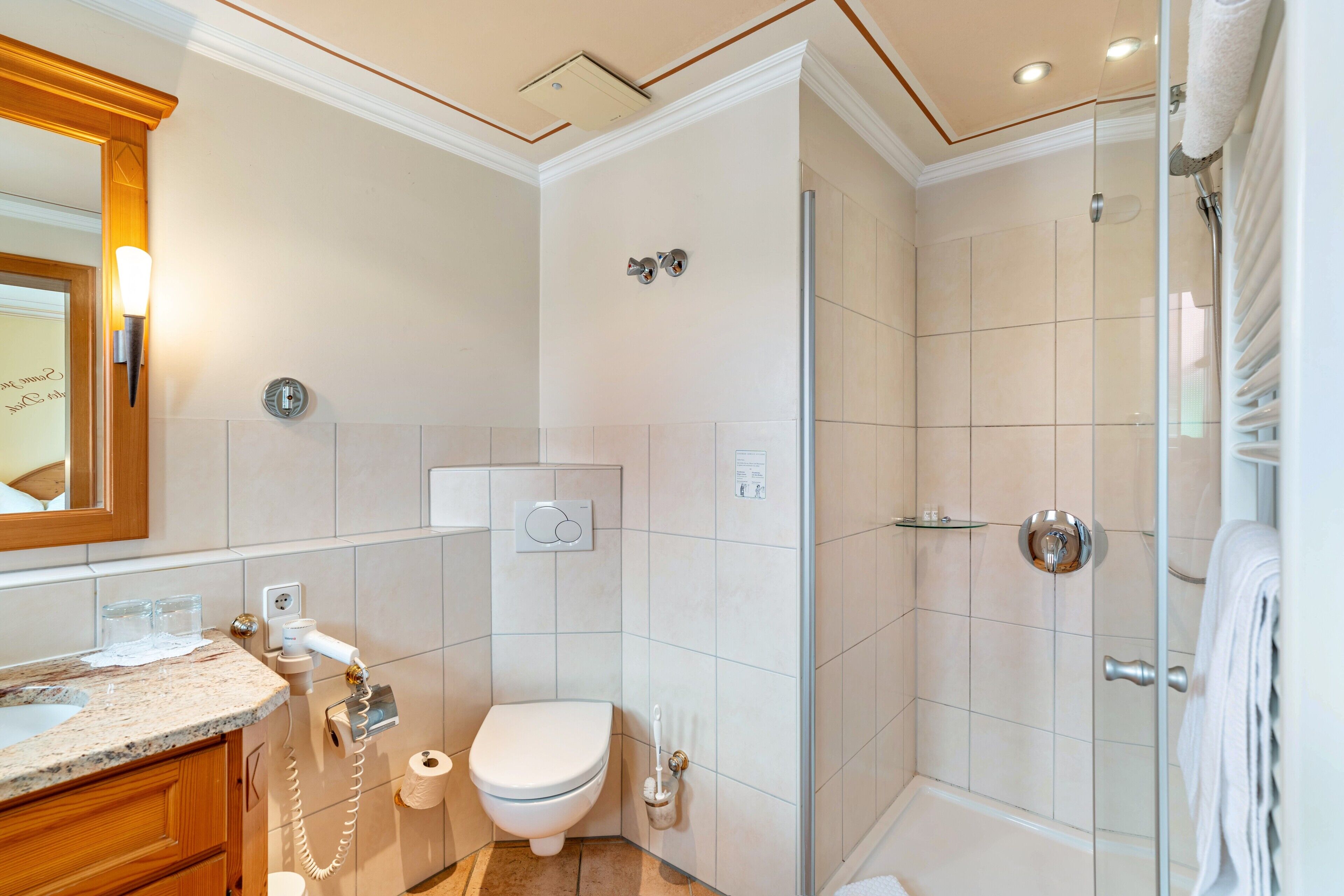 Une salle de bain comprenant des toilettes, un lavabo, une douche et un espace de douche séparé par des parois en verre.
