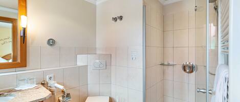 Une salle de bain comprenant des toilettes, un lavabo, une douche et un espace de douche séparé par des parois en verre.