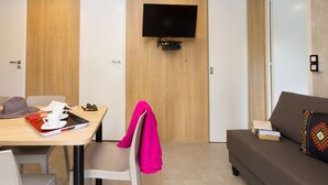 Una habitación de hotel moderna con comedor, sofá y televisor de pantalla plana en la pared.