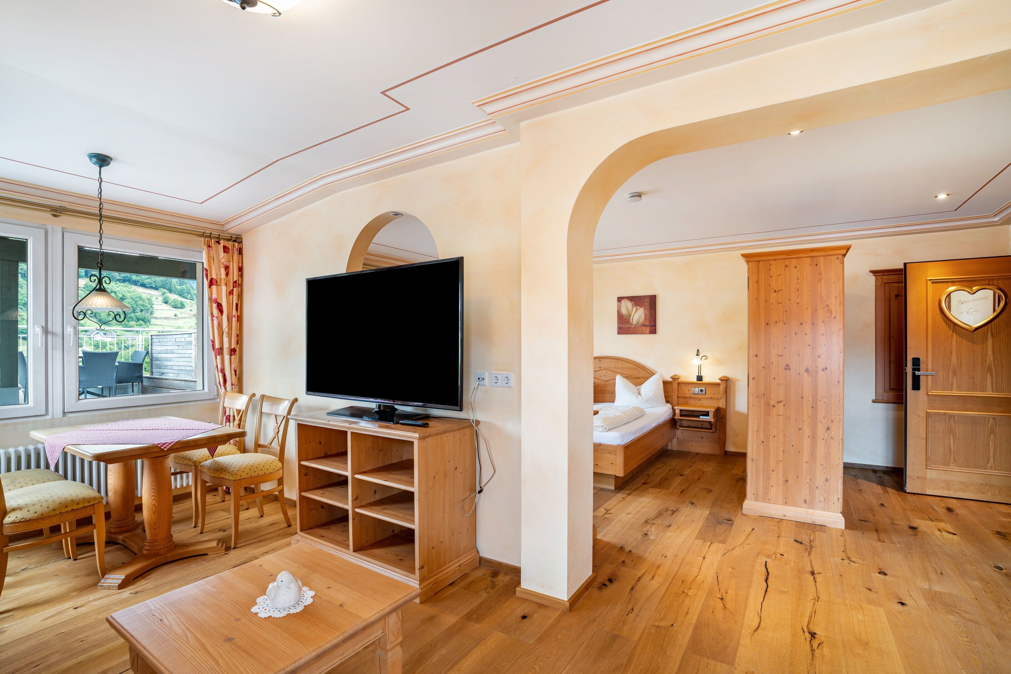 Une chambre dotée d’une télévision, de meubles en bois, d’un lit et offrant une vue sur l’extérieur.