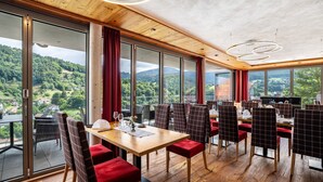 Un restaurante con una mesa y sillas amplias, ventanas grandes con vistas a un área boscosa y un techo de madera.